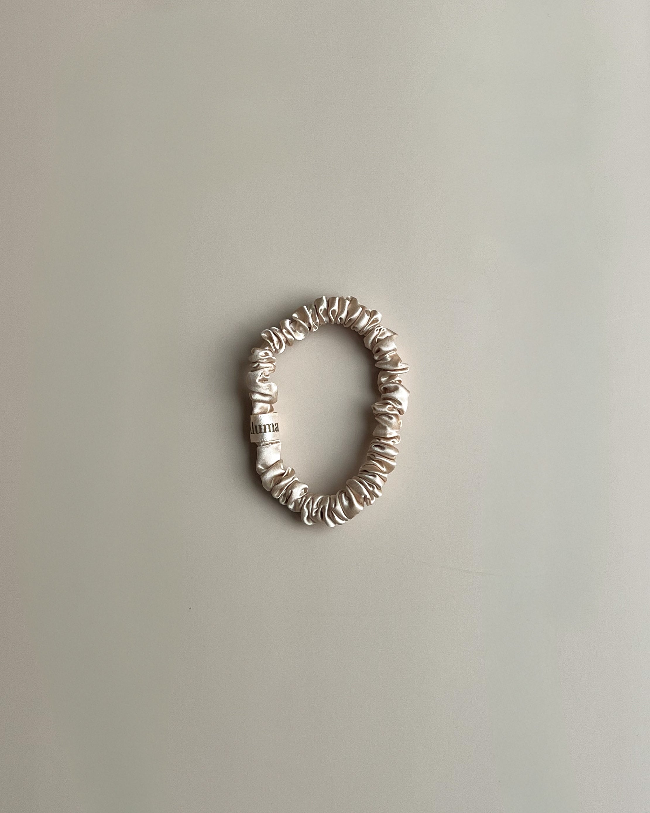 Silke scrunchie 1 cm fra Aluma Bloom i Sunbeam Sand sandbeige, GOTS-certificeret mulberry silke hårelastik på neutral beige baggrund