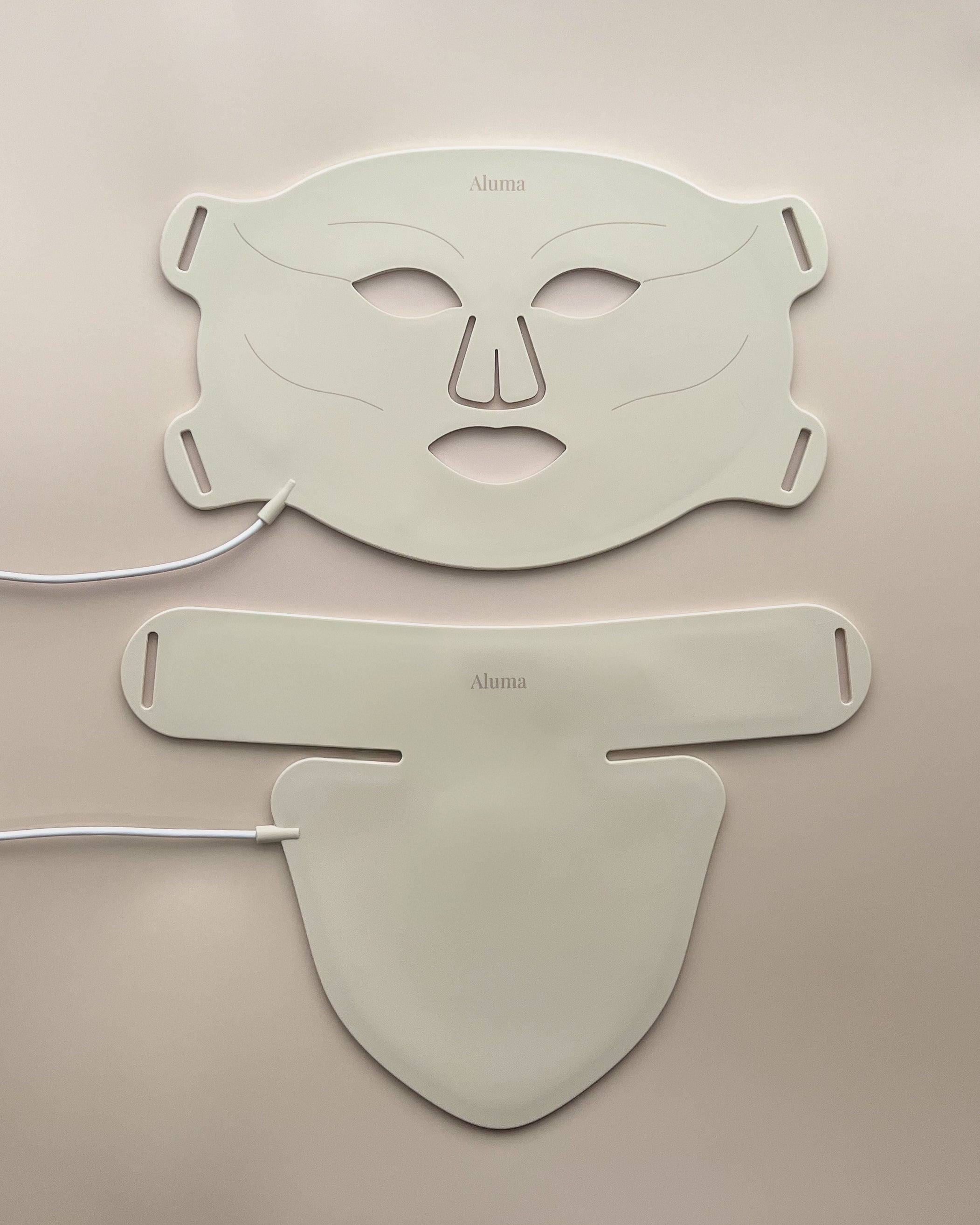 Aluma Aurora LED-maske til ansigt og hals lagt fladt på beige baggrund med begge dele og hvide kabler synlige