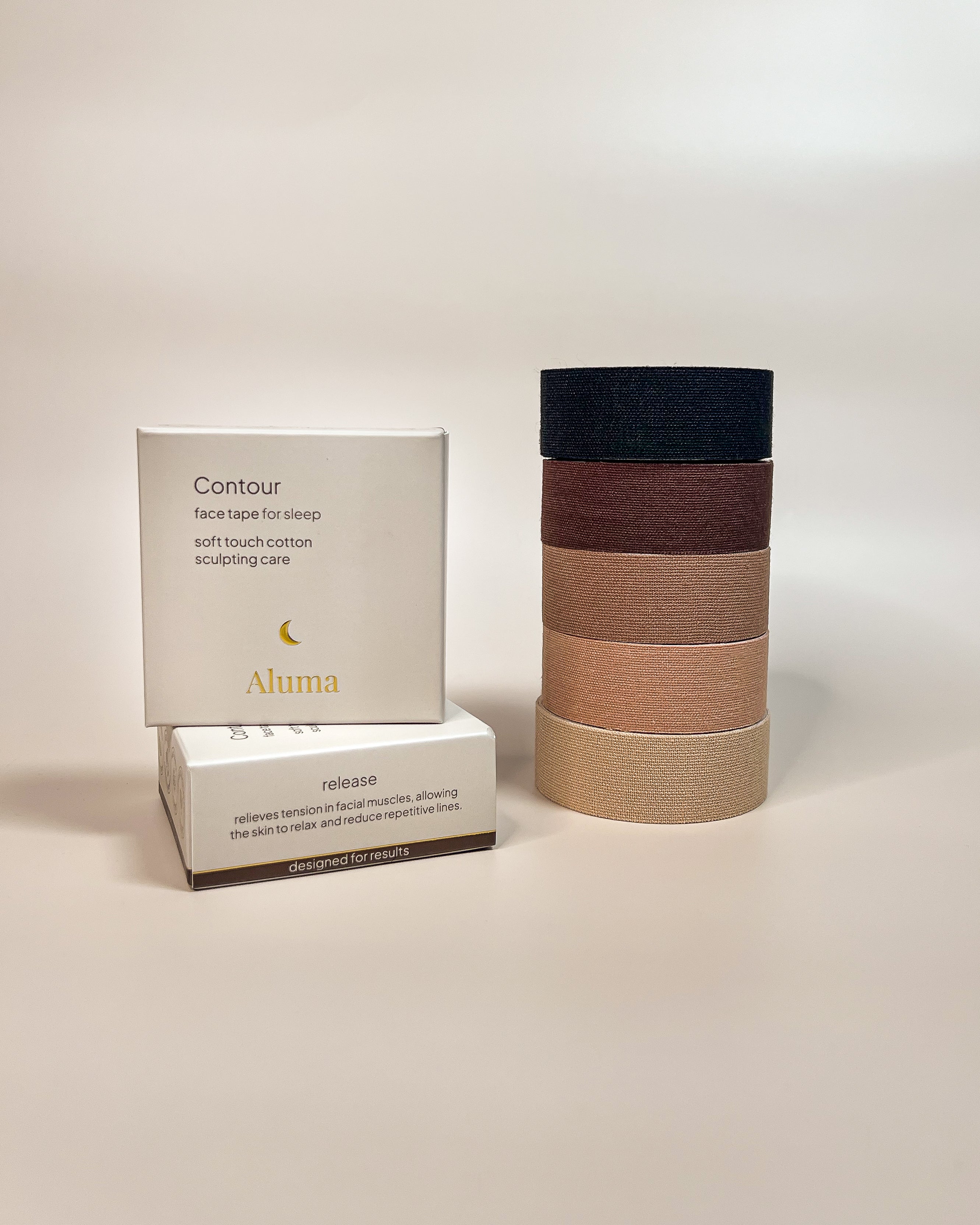 Aluma Contour face tape for sleep packaging shown with a vertical stack of tape rolls in four shades on a soft beige background.