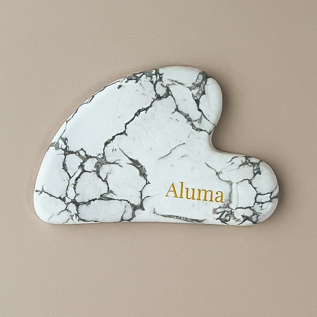 Yin gua sha i hvid turquoise fra Aluma på beige baggrund.