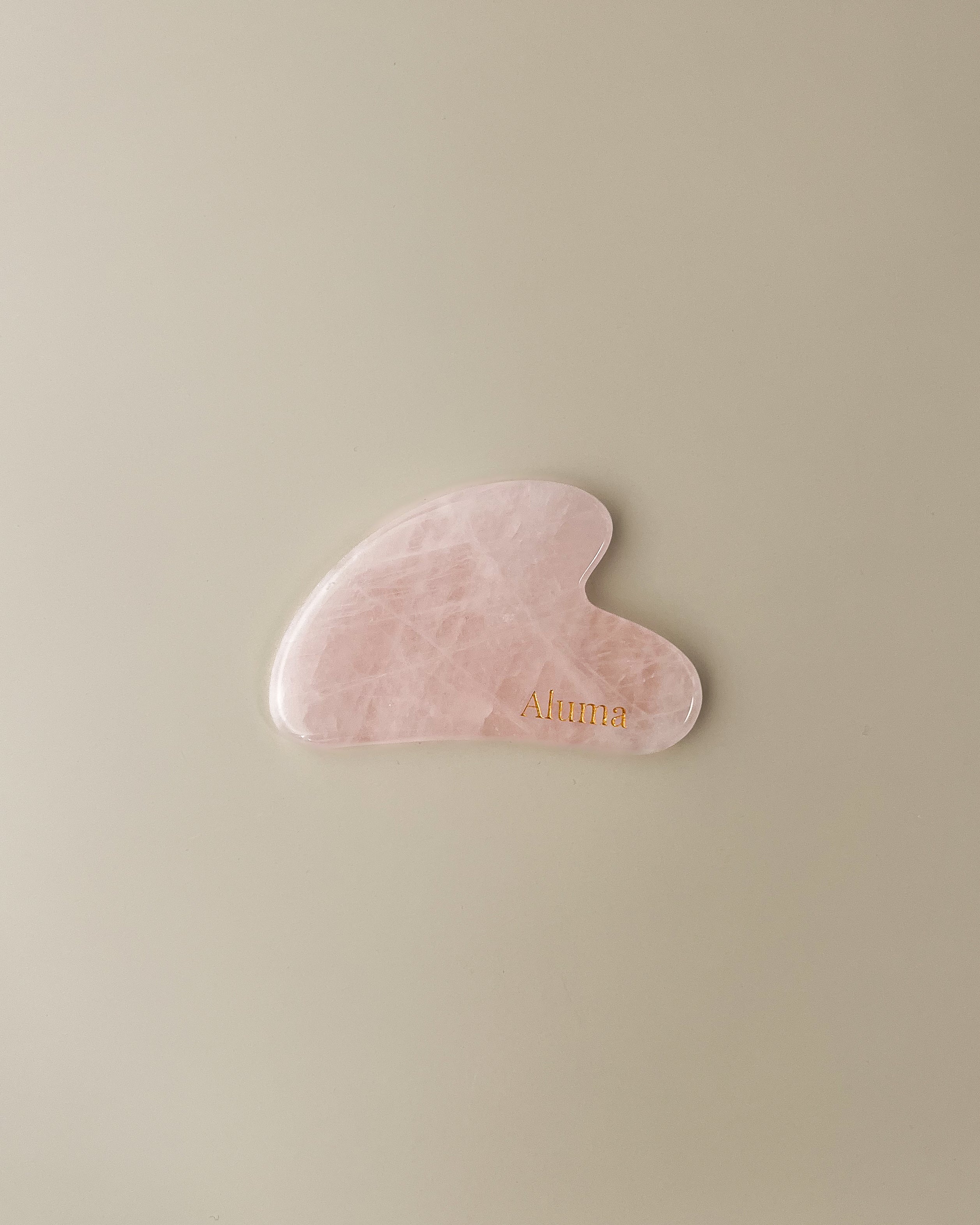 Yin gua sha i rosa kvarts fra Aluma på beige baggrund, blid ansigtsmassage sten til glød, lymfedrænage og slow aging ritualer.