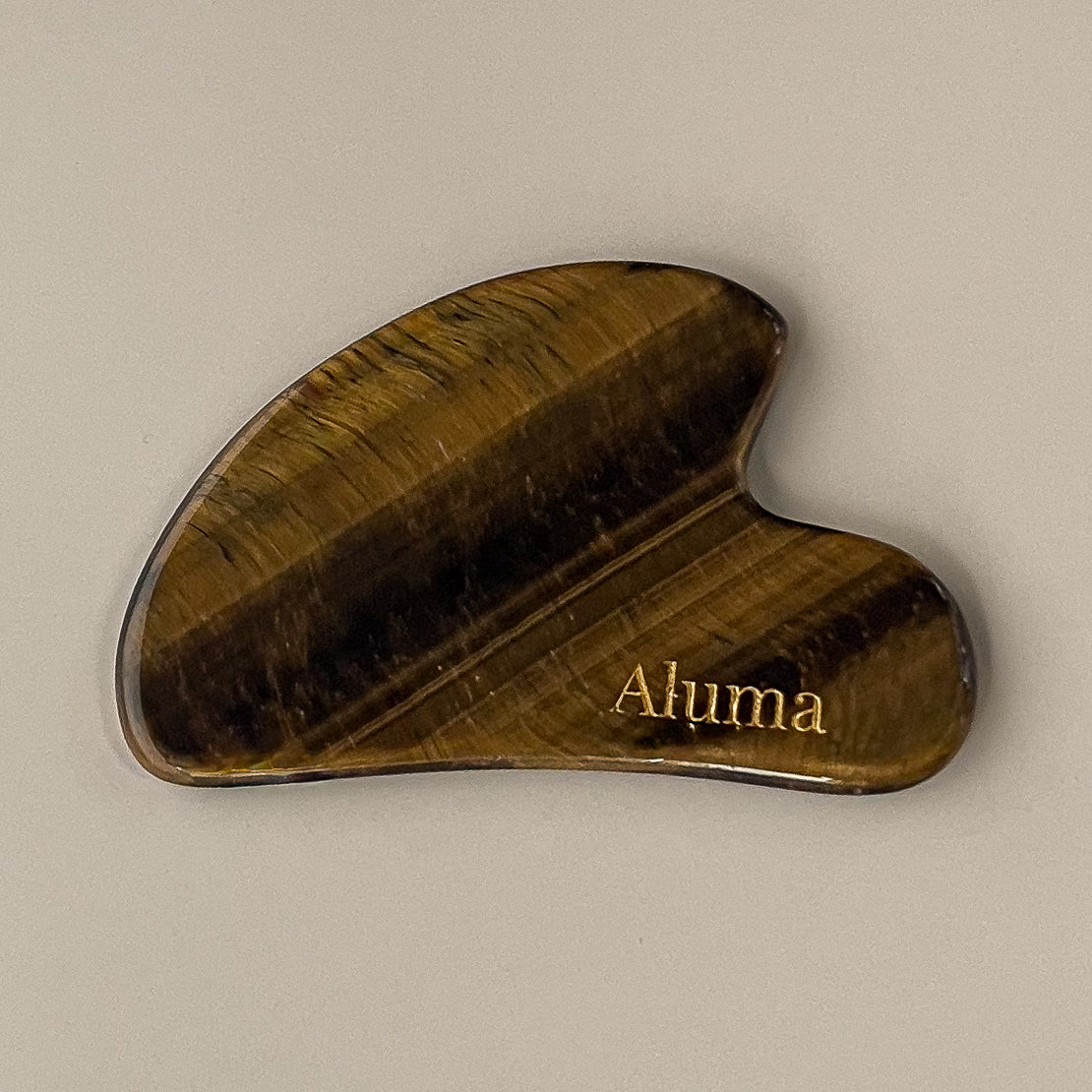 Yin gua sha i tiger eye stone fra Aluma på beige baggrund.