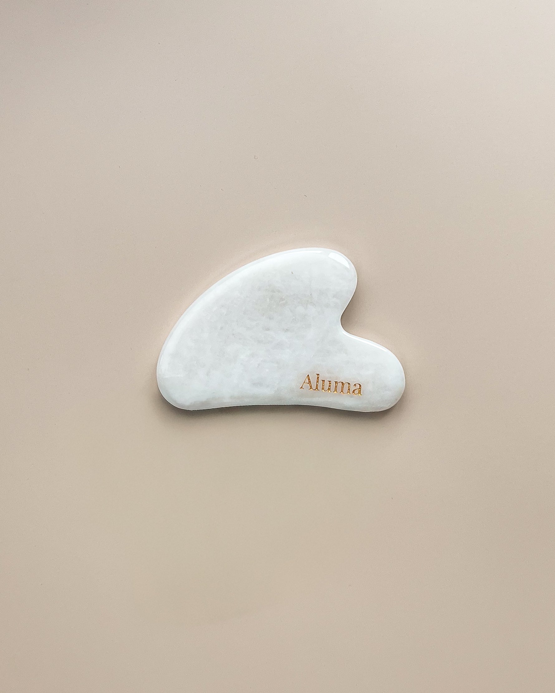 Yin gua sha i hvid jade fra Aluma på beige baggrund, elegant ansigtssten til daglig gua sha massage.