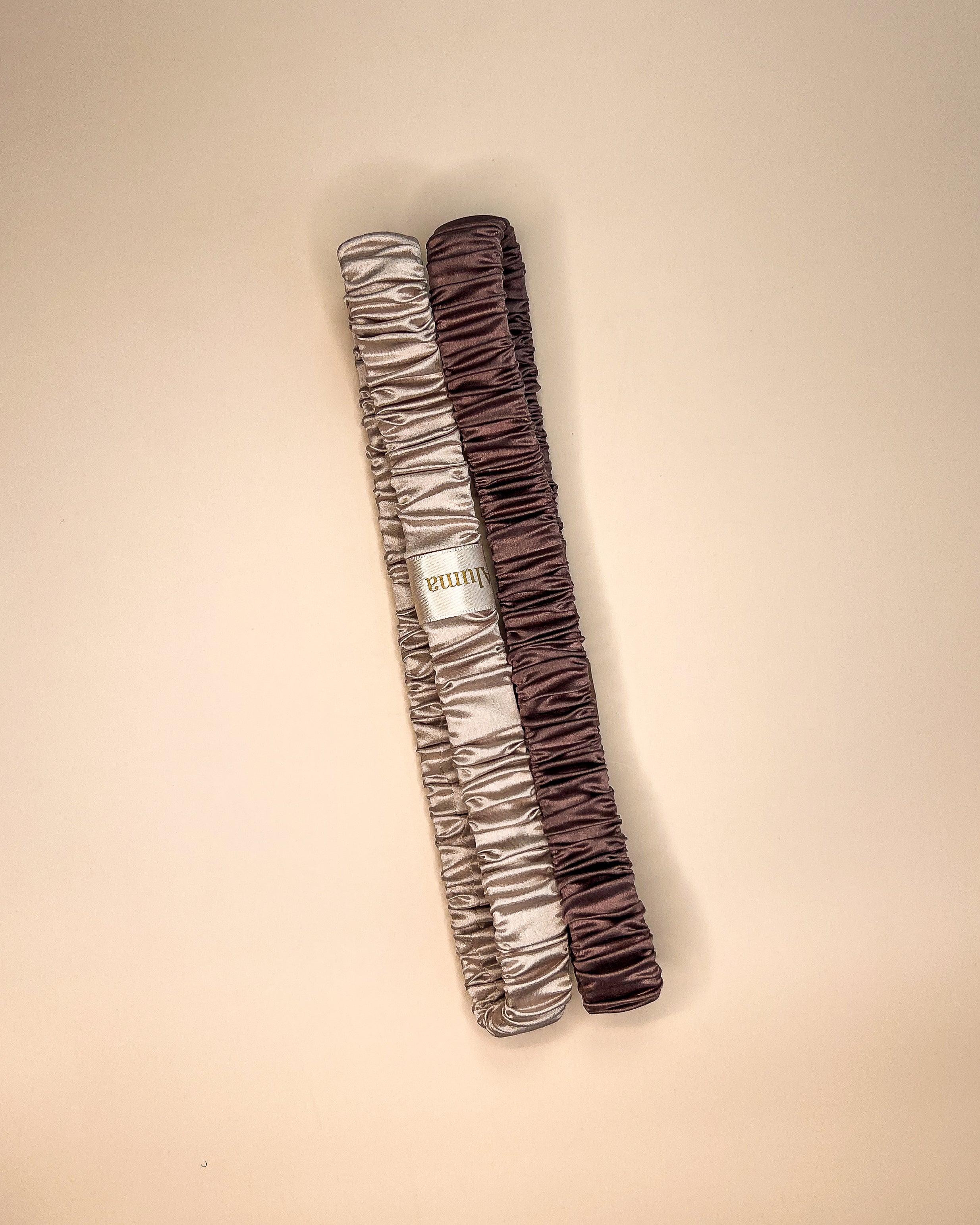 To Aluma Loop elastiske silke hårbånd i calm cacao og violet whisper, lagt side om side på beige baggrund 