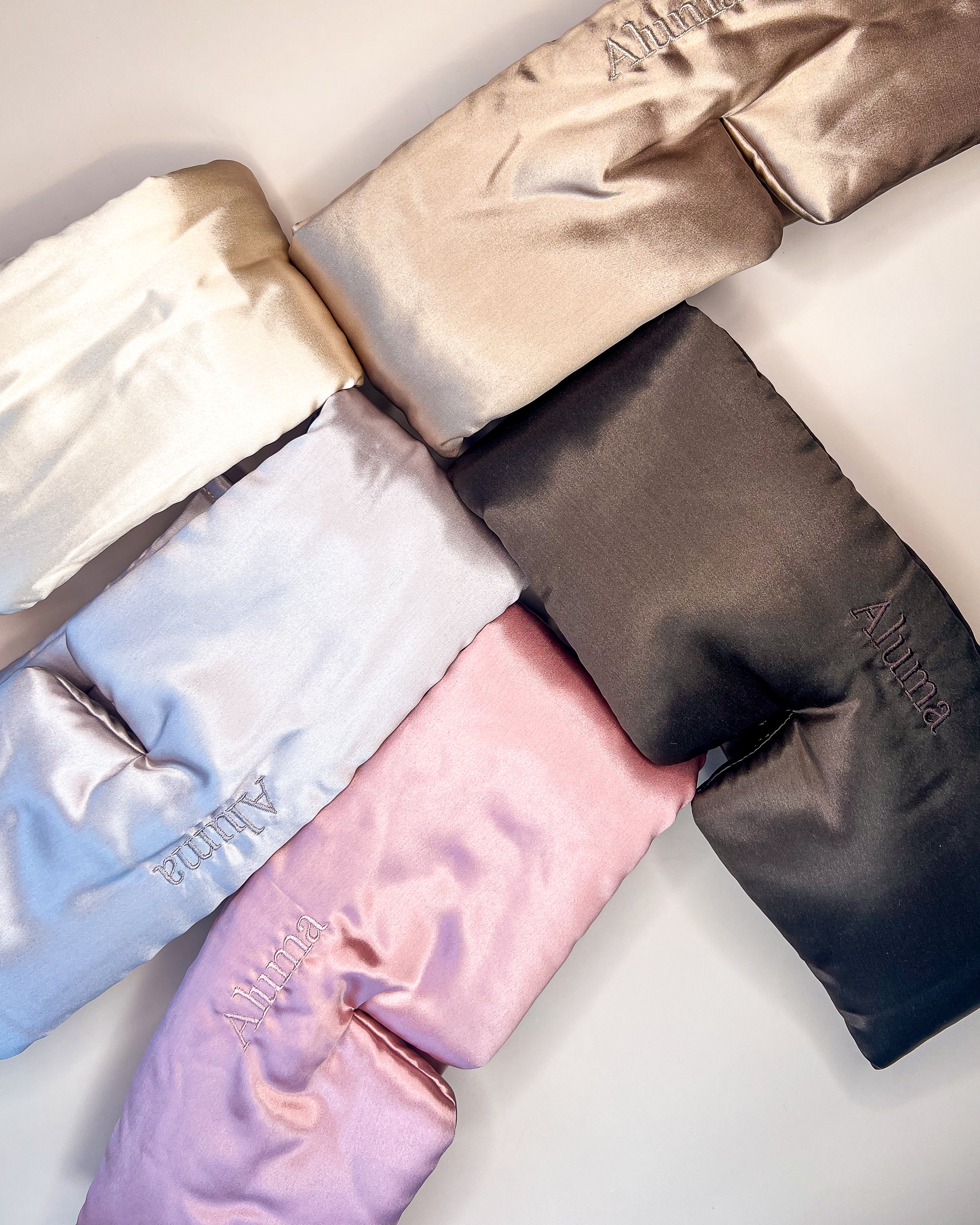 Flatlay med fem Aluma silke-søvnmasker i lyse og mørke nuancer, arrangeret i en cirkel på lys baggrund